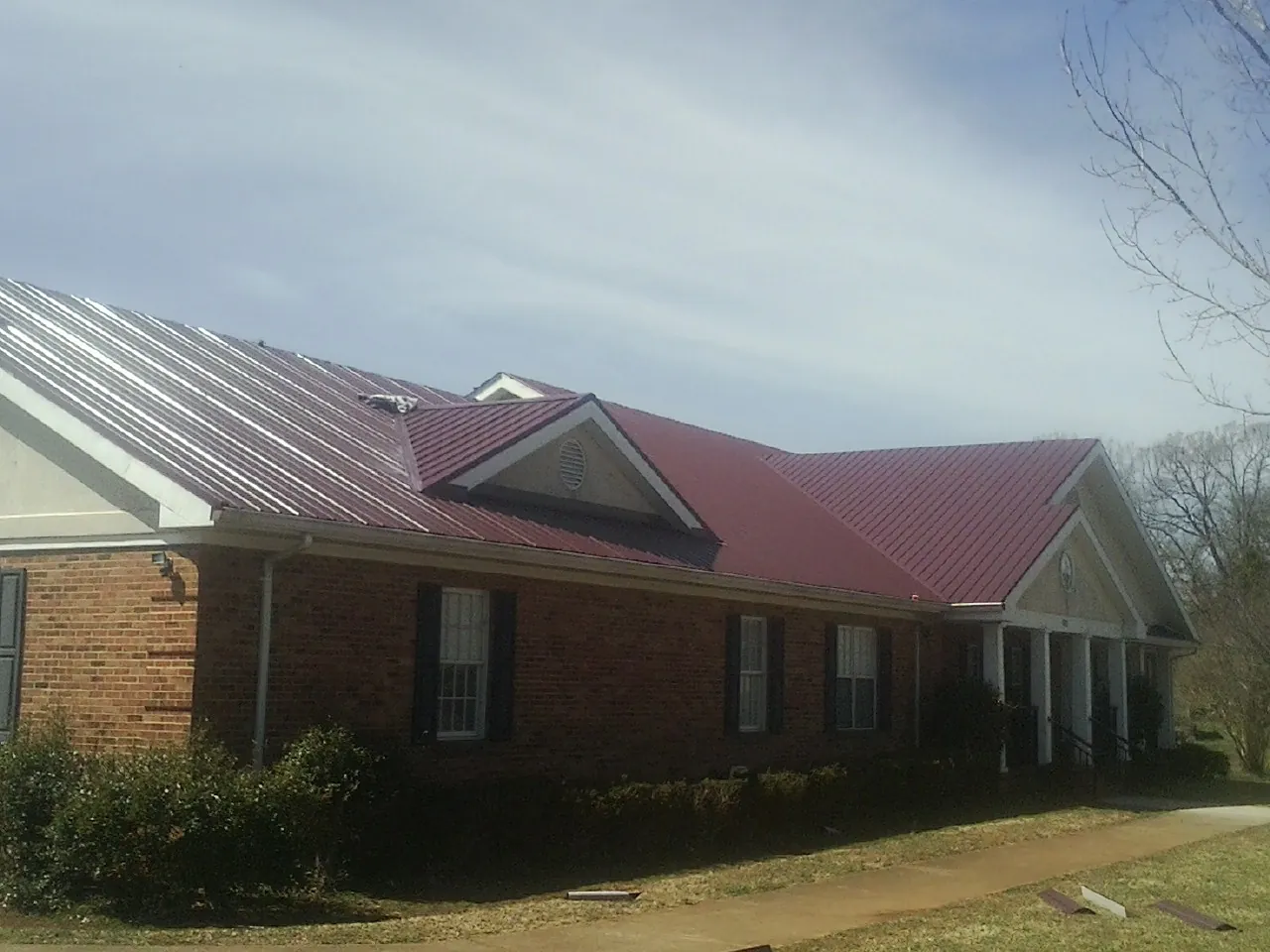 Red metal roof with gabled entries on a long brick building, from a Hail Damage Roof Repair job in Danbury